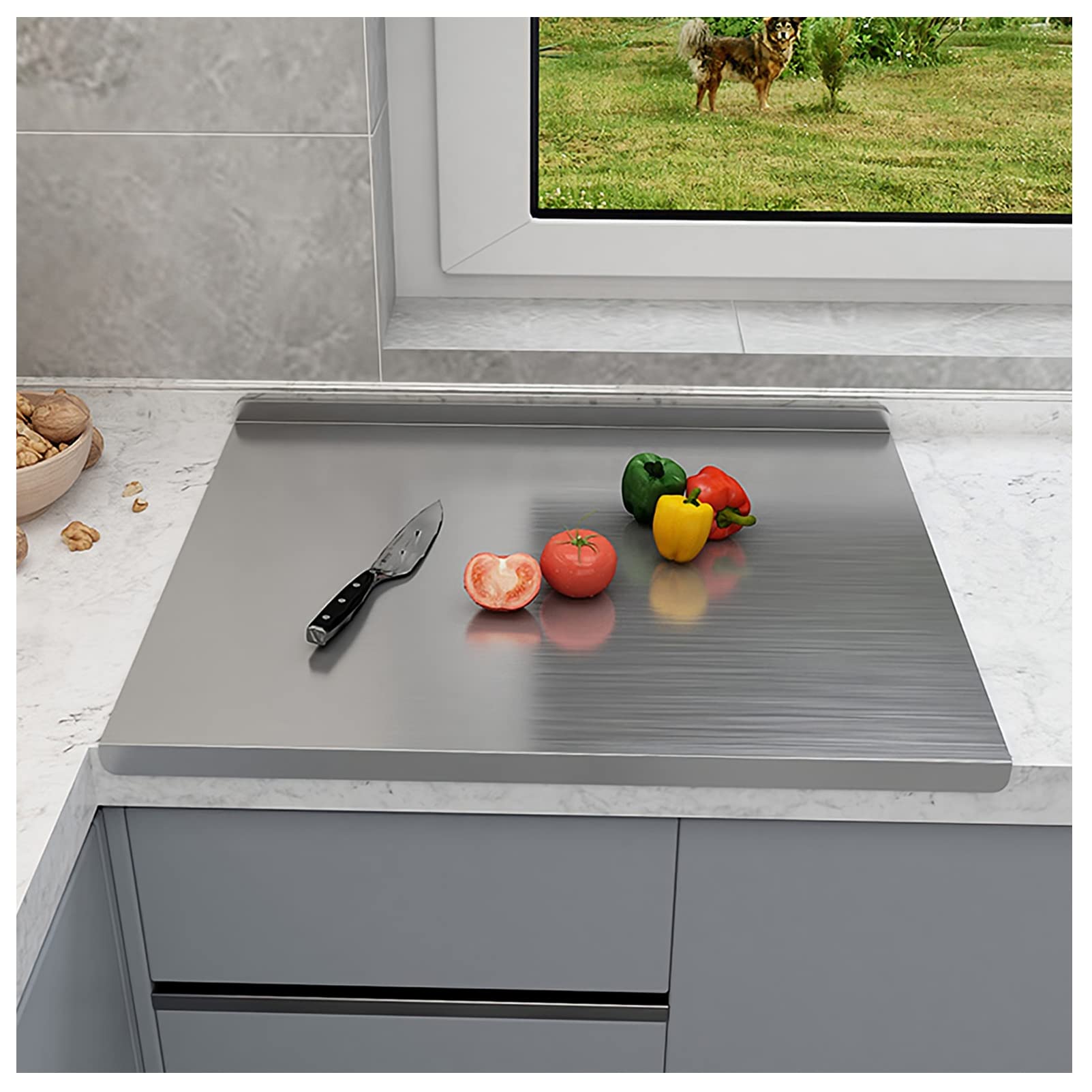 Stainless steel cutting board with a knife and vegetables on a kitchen counter.